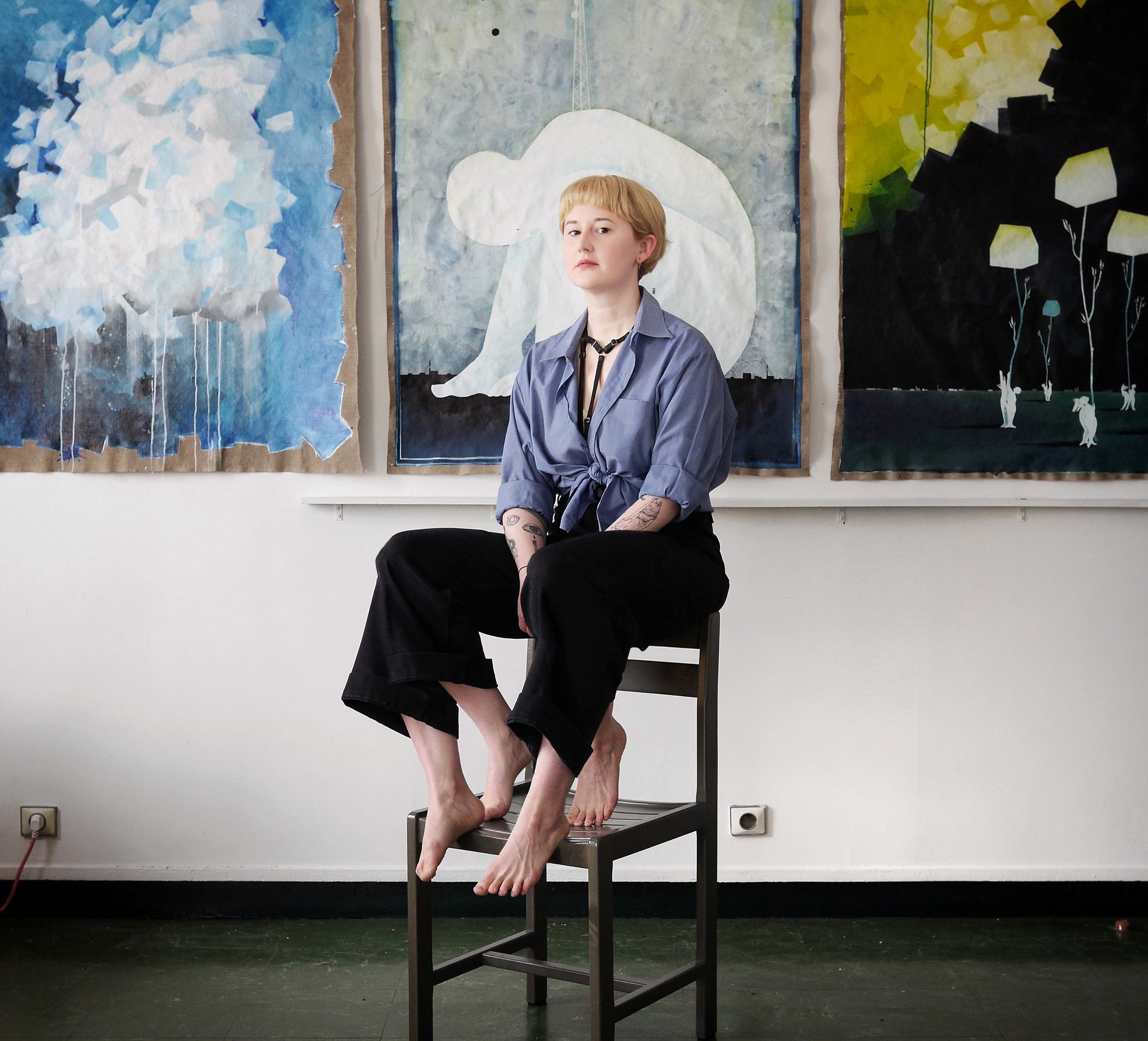 Selbstporträt der Künstlerin Anna Kohlweis mit vier Beinen, während sie vor modernen Malereien auf einem Hocker sitzt