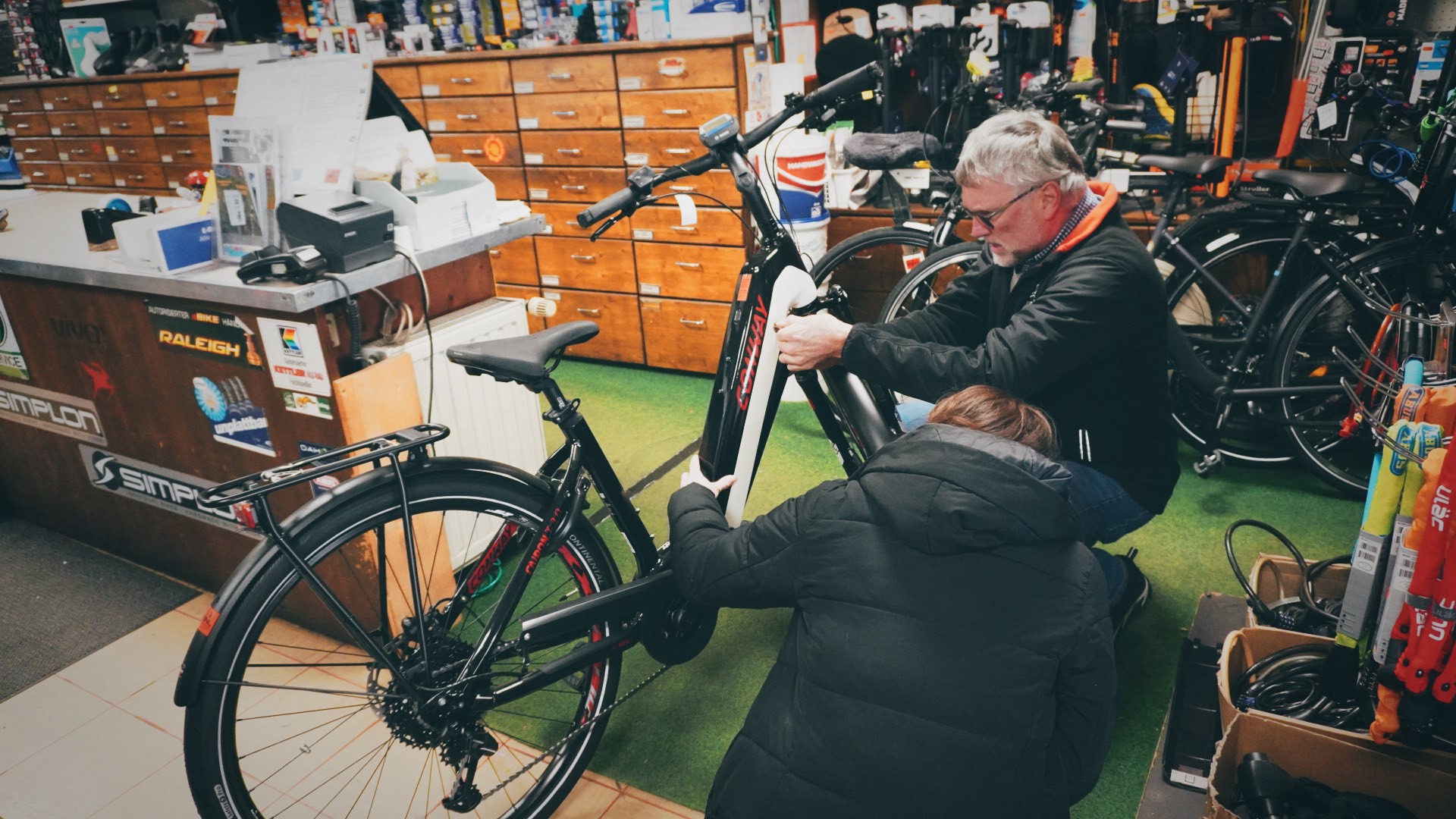 Michael Beinl, Chef von Zweirad Beinl, hockt in seinem Geschäft mit einem Kunden vor einem Rad 
