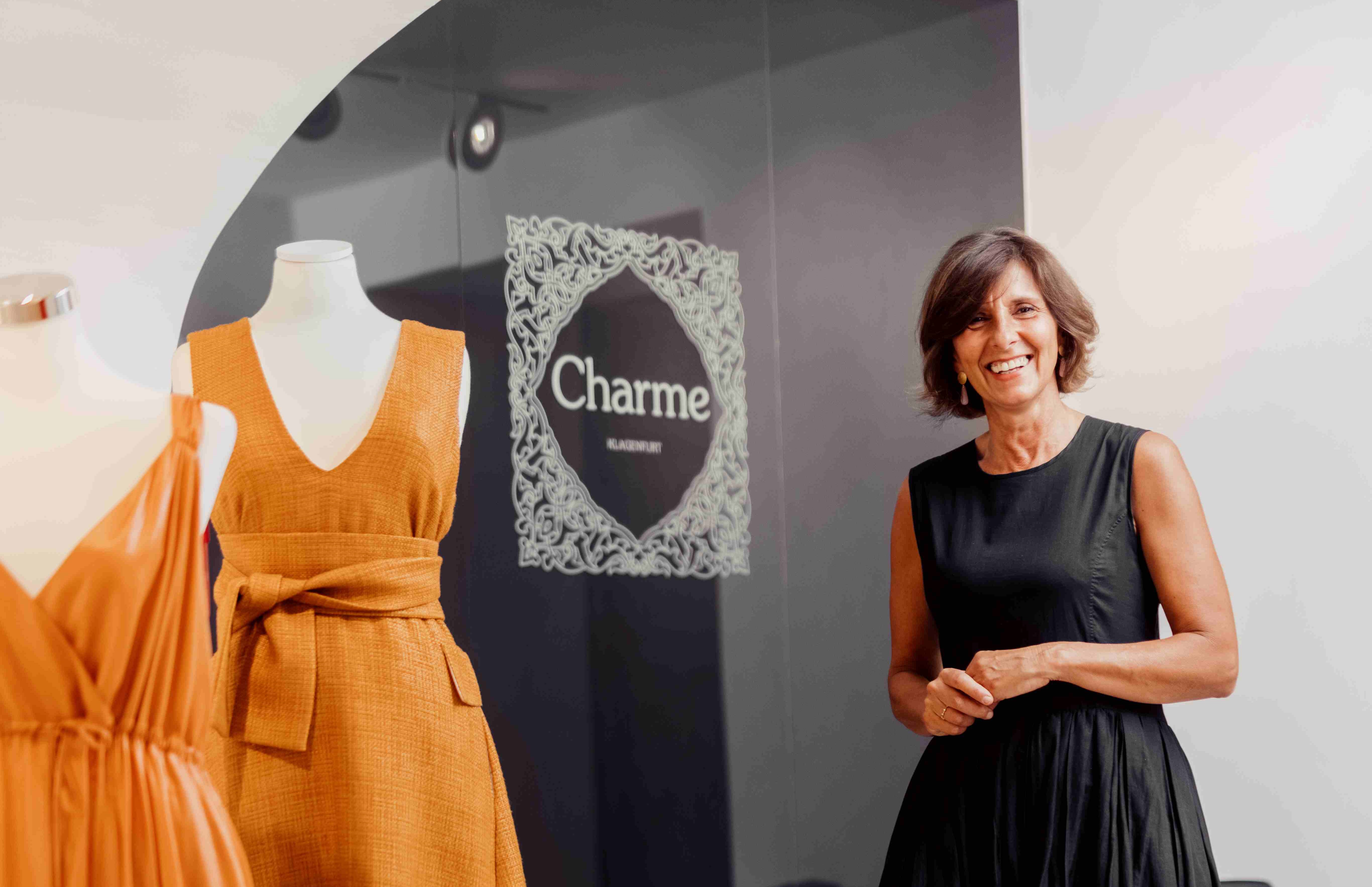 Boutiquen inhaberin Brigitte Guagliardi im Verkaufsraum ihres Geschäfts mit zwei sonnengelben Kleidern an Schaufensterpuppen vor sich