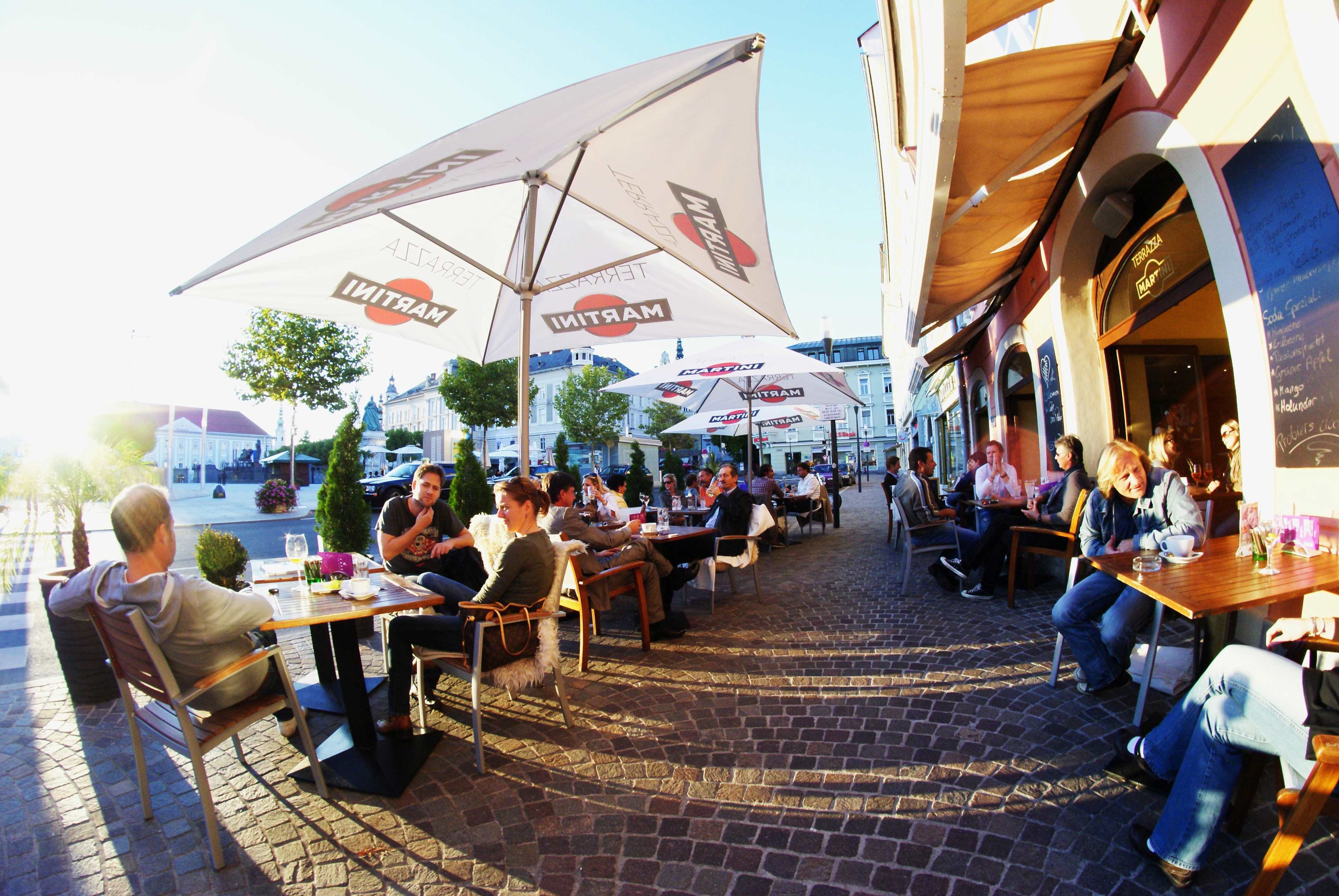 Ansicht des gut bevölkerten Gastgartens vom Cafe am Platz in Klagenfurt in der Abendsonne