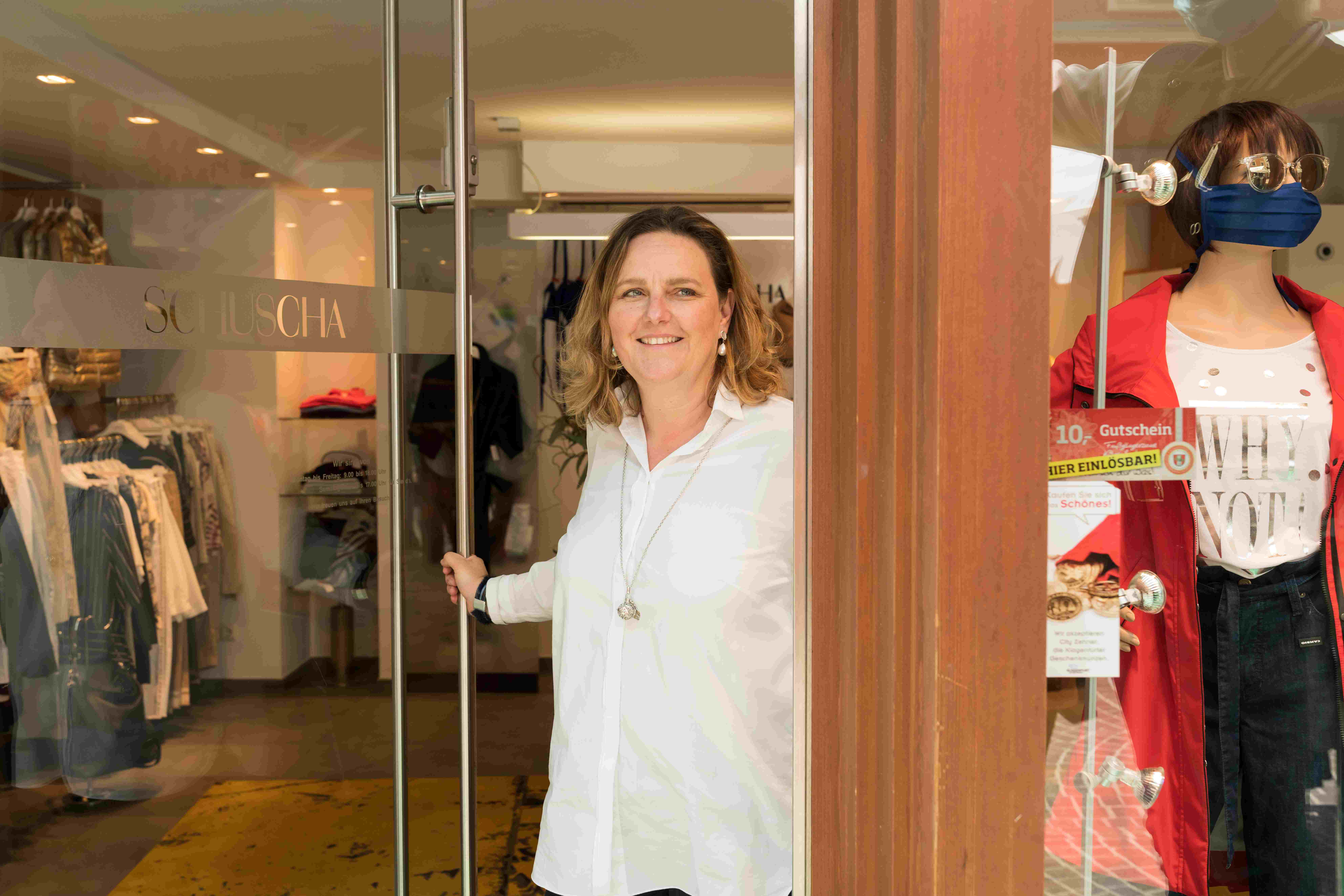 Frau Lesjak-Schuscha steht in der Glastür ihrer Boutique und lächelt in die Kamera