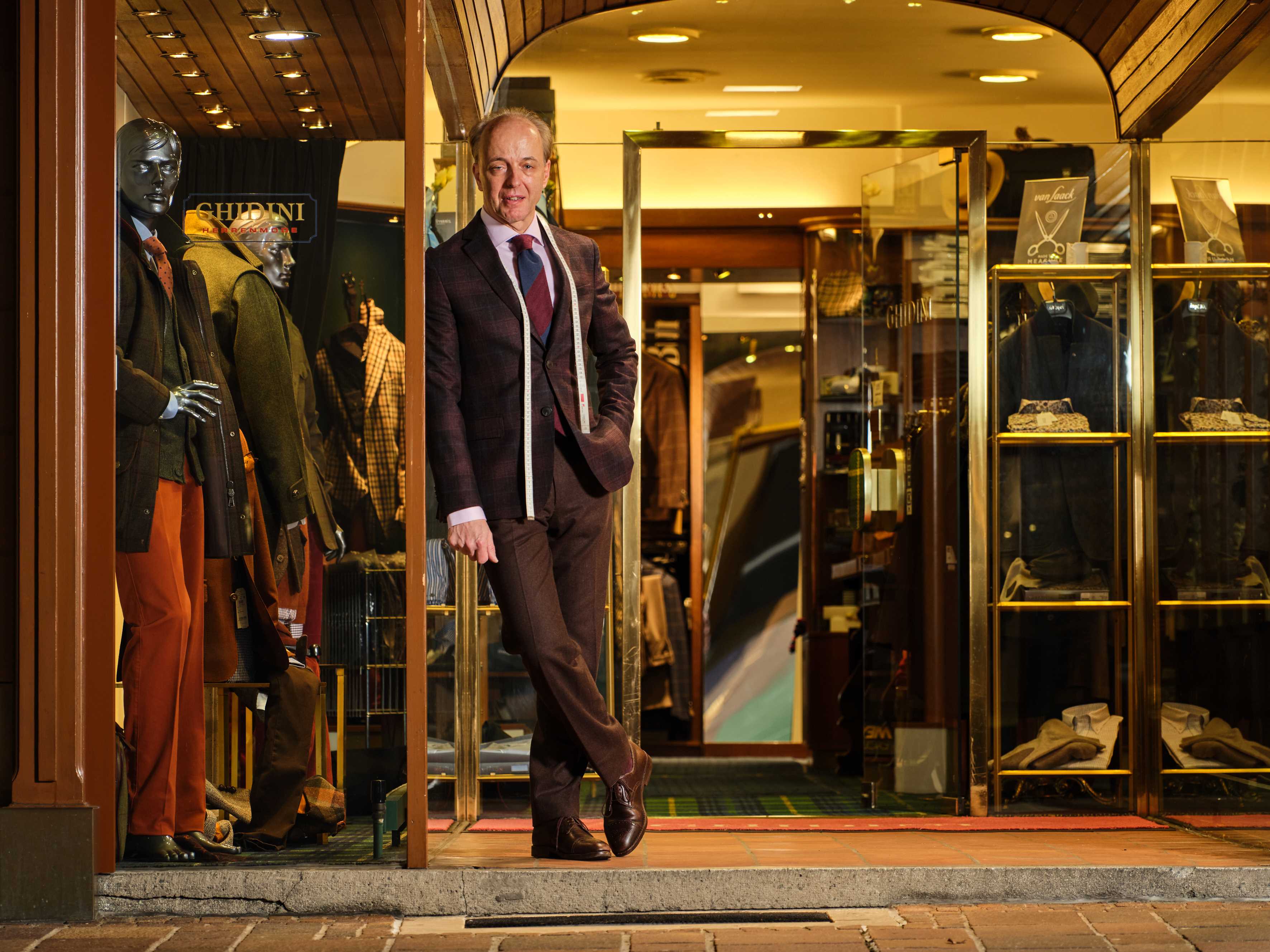 Angelo Ghidini lehnt im schicken Anzug vor dem Eingang zu seiner Herrenausstatter-Boutique