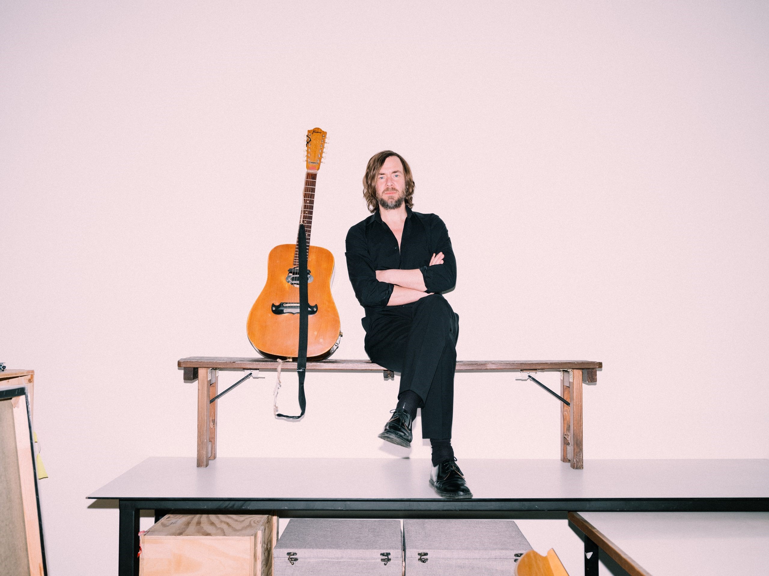 Portrait von Herwig "Fuzzman" Zamernik auf Holzbank sitzend mit Akustikgitarre an Wand angelehnt 