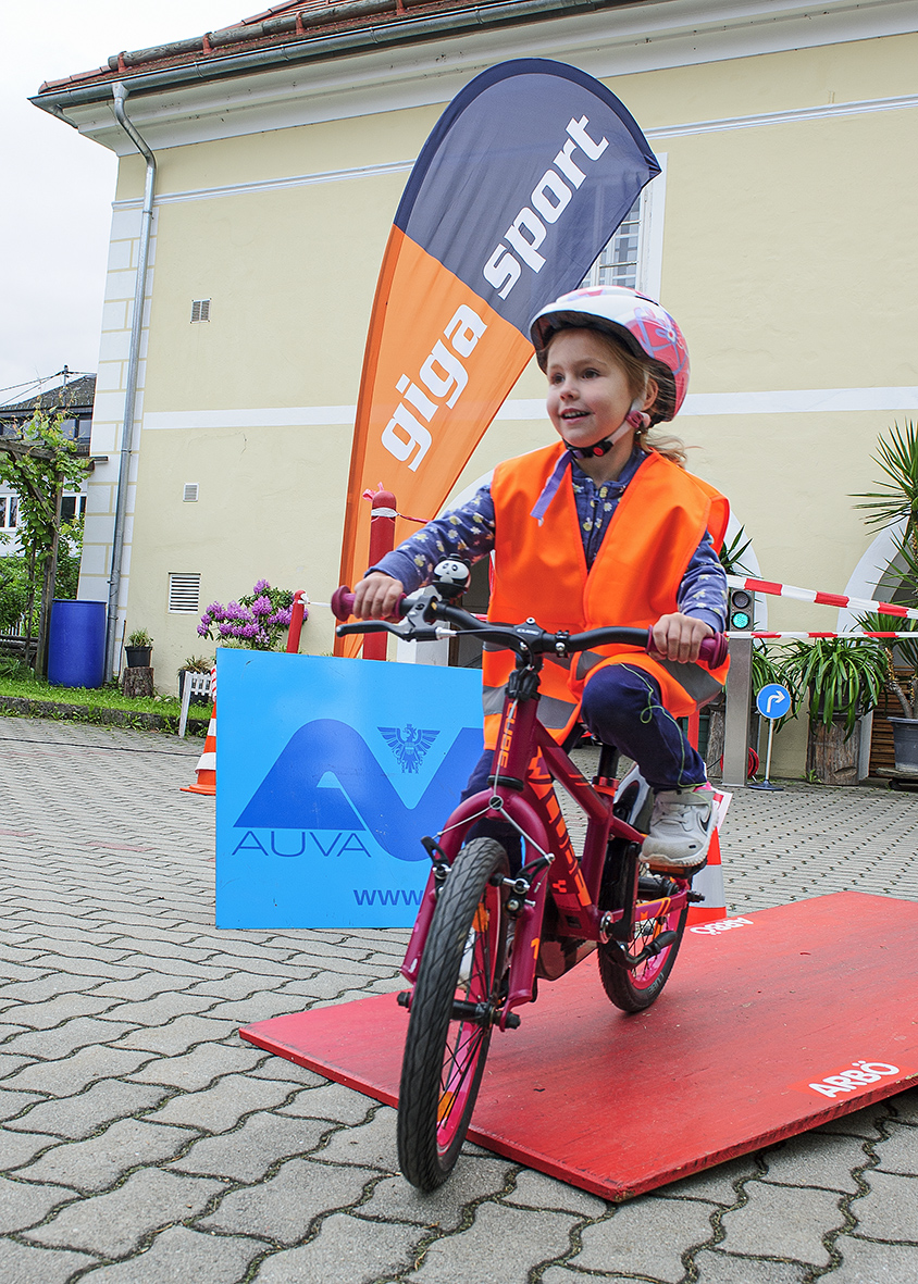 Kind mit oranger Warnweste auf einem roten Rad